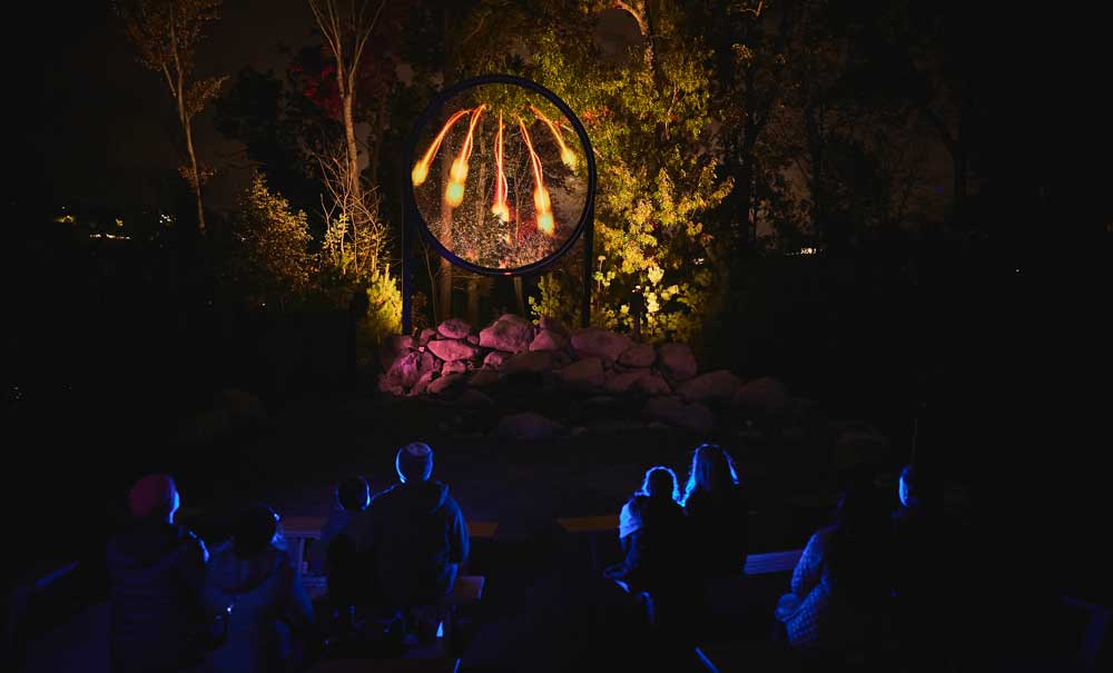 A group of individuals seated in darkness, captivated by a large, glowing sculpture in front of them.