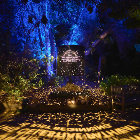 Nighttime garden display with projected celestial imagery and text, including "Your journey along the celestial pathway is a new beginning".